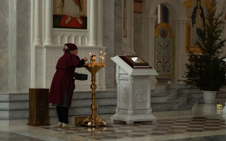 A woman is lighting candles in a beautifully decorated church, with religious icons and antique structures.