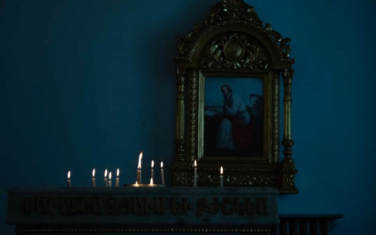 Dimly lit church interior with ornate religious painting and candles.