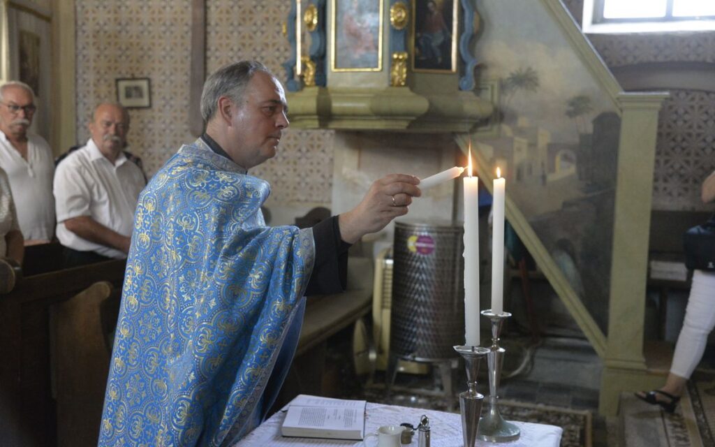 A priest in a church lighting candles during a religious ceremony with attendees observing.