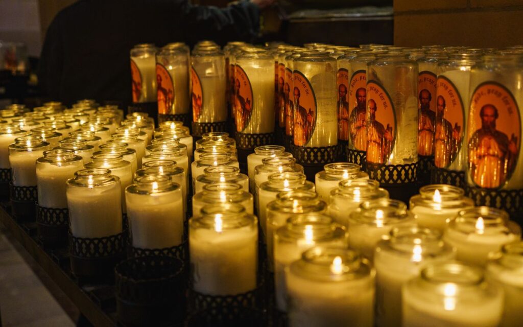 Rows of glowing prayer candles in a church create a warm, solemn atmosphere.