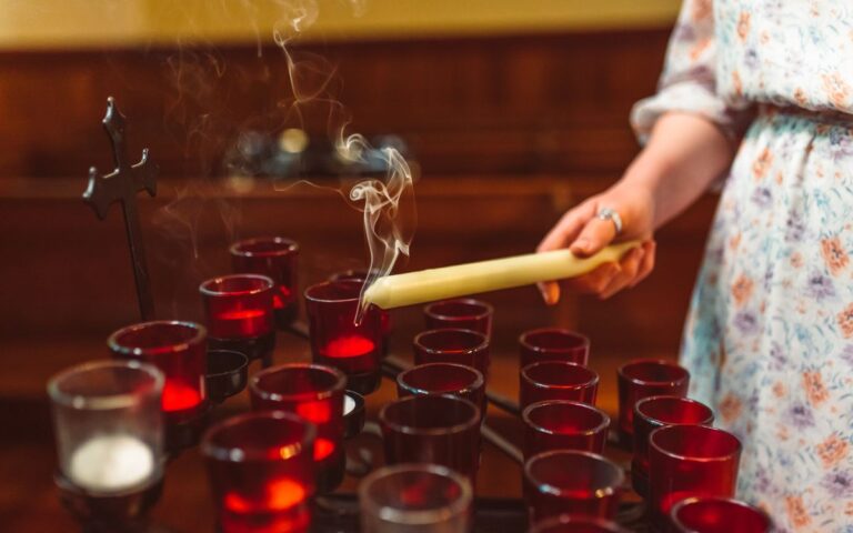 A close-up of a hand lighting church candles with gentle smoke rising.