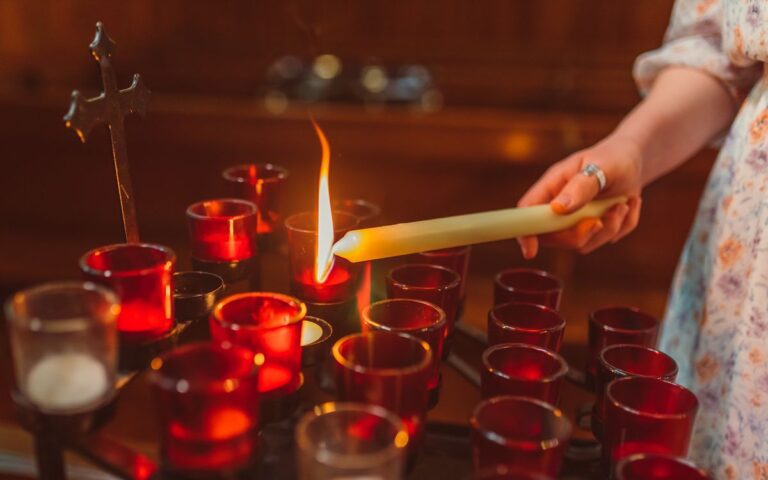 A close-up of a person lighting a candle in a church with red candle holders.