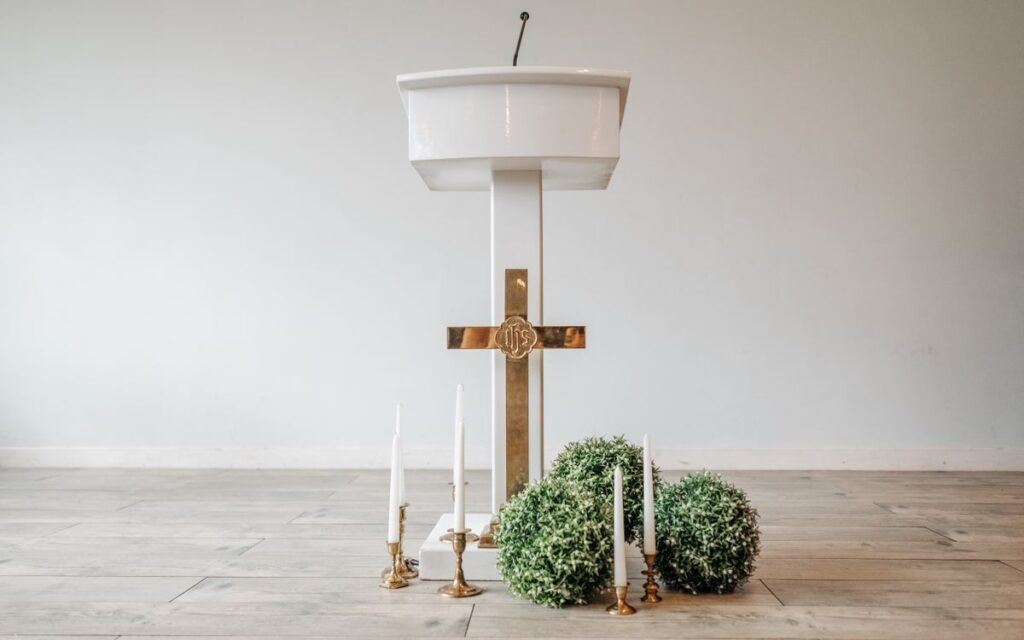 A minimalistic church altar setup featuring a white podium, golden cross, and decorative candles.