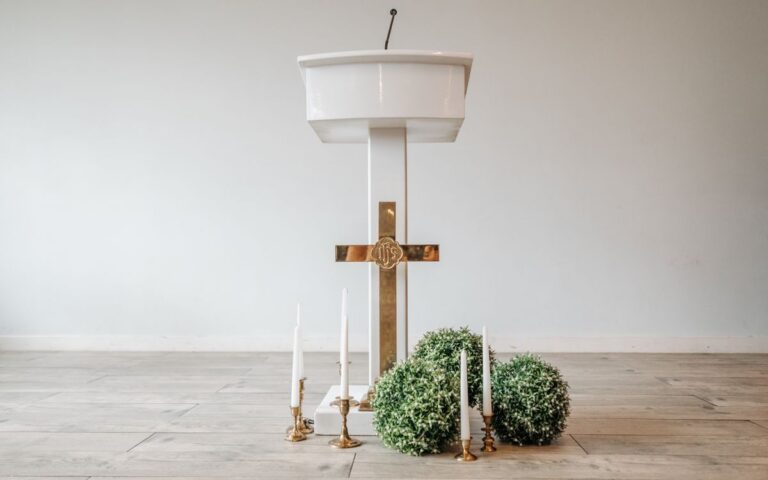 A minimalistic church altar setup featuring a white podium, golden cross, and decorative candles.