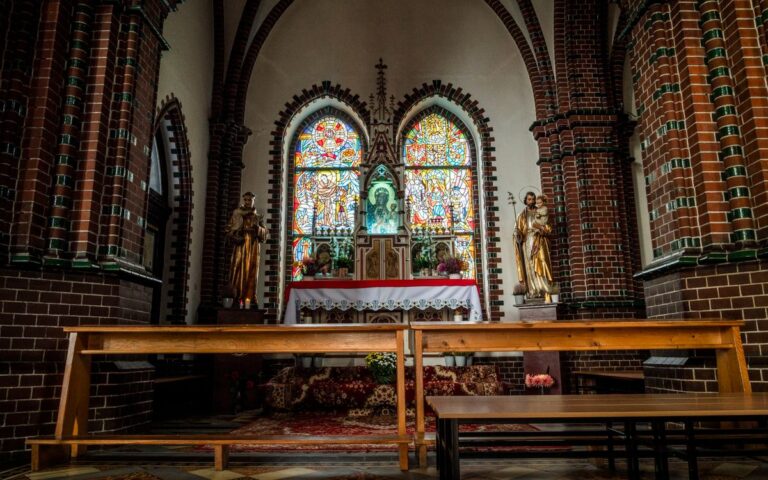 A serene view of a church altar featuring stained glass and statues.